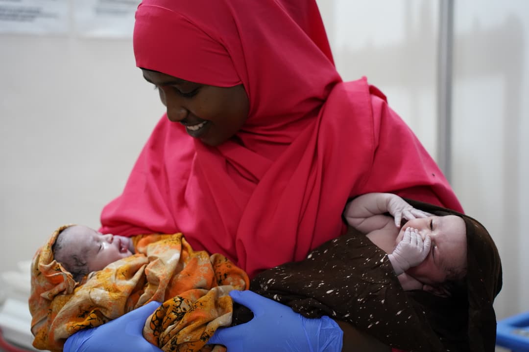 A midwife smiles as she holds healthy newborn twins